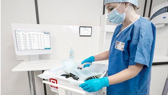 Medical professional in scrubs preparing equipment with monitors displaying data in the background.