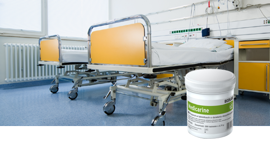 Hospital room with two empty beds with yellow side panels and a 'Medicarine' disinfectant container in the foreground.